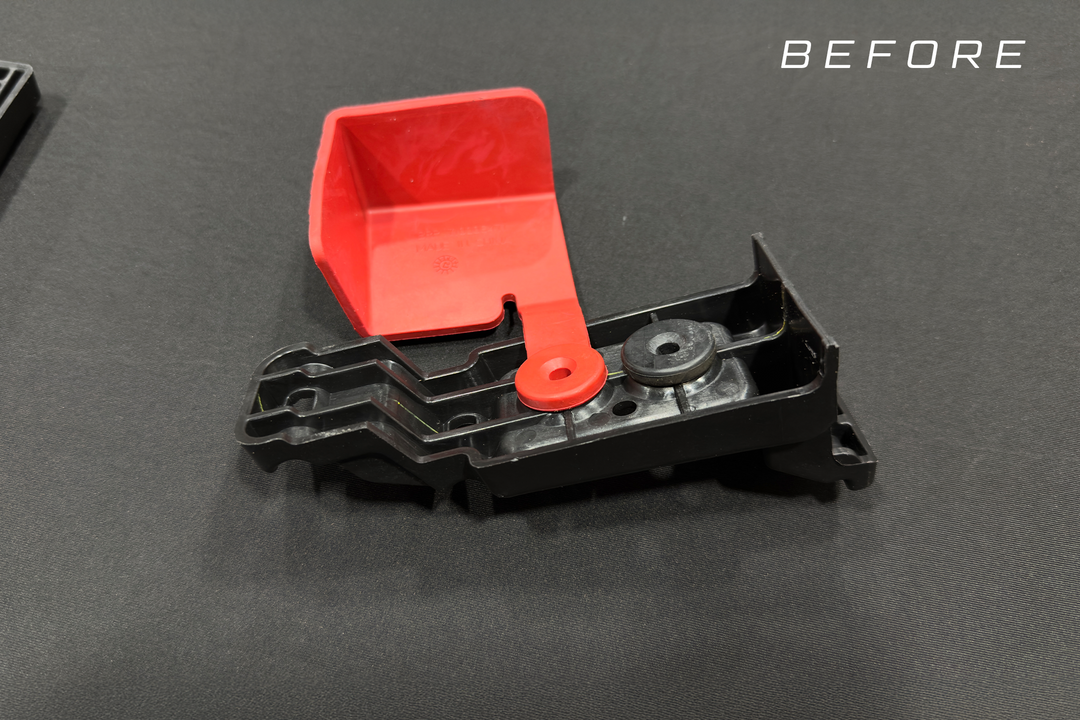 Black plastic automotive bracket with attached red protective cover