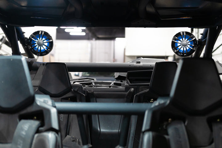Two circular marine speakers with blue LED lighting mounted on the roll cage of an off road vehicle