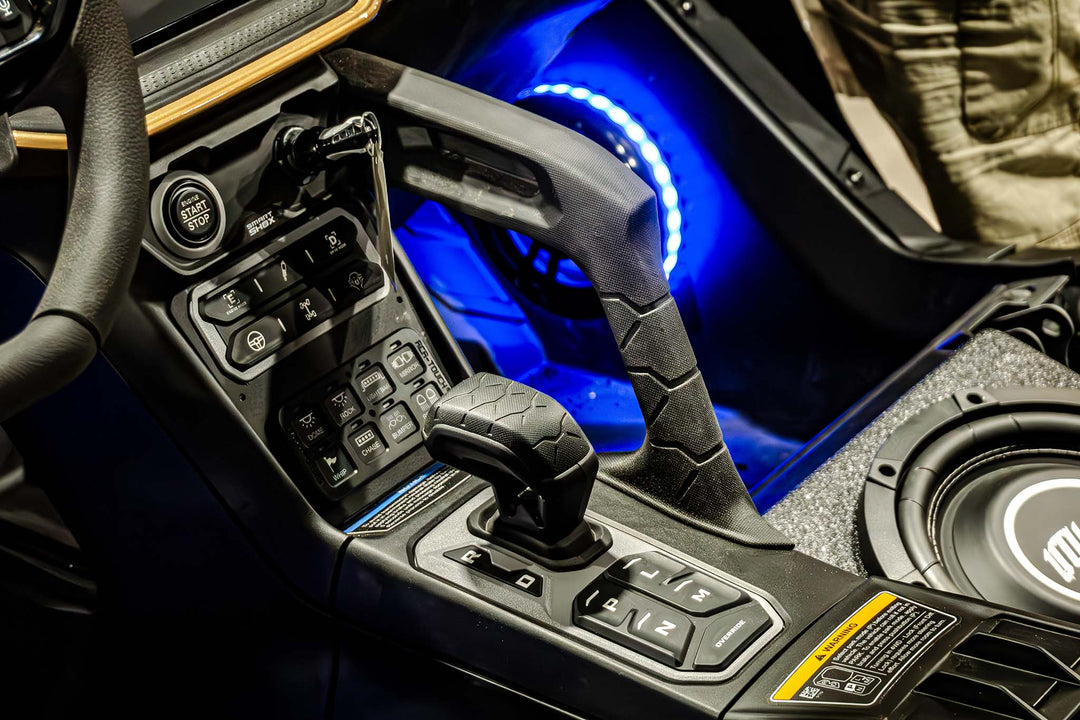 Center console of a vehicle with gear shifter, start button, and illuminated blue speaker